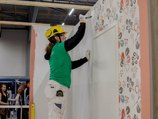 Taitaja2023 Espoo -kilpailun maalaus ja tapetointi -lajin kultamitalisti Camilla Laukkanen tapetoi seinää. Kuva: Ksenia Shurygina, Omnia / Skills Finland